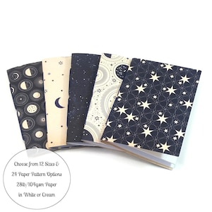 May include: Five small notebooks with different celestial patterns on the covers. The covers are black with white stars, moons, and sun designs. The text on the bottom reads "Choose from 12 Sizes & 24 Paper Pattern Options 28lb/104gsm Paper in White or Cream."