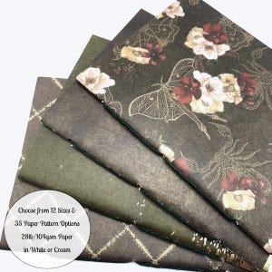 May include: A stack of notebooks with various patterned covers. The top notebook features a dark background with floral and insect illustrations. The text on the bottom left says, "Choose from 12 Sizes & 35 Paper Pattern Options 28lb/104gsm Paper in White or Cream."