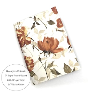 May include: A rectangular notebook featuring a white cover with a repeating pattern of rust-colored roses and muted green leaves. A circular white label includes the text: Choose from 12 Sizes & 34 Paper Pattern Options 28lb/104gsm Paper in White or Cream.