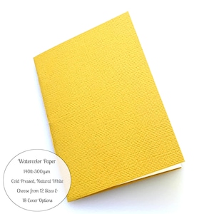 May include: A yellow watercolor paper notebook with a textured cover. The notebook is closed and the cover is folded over. The text on the cover reads "Watercolor Paper 140lb 300gsm Cold Pressed, Natural White Choose from 12 Sizes & 18 Cover Options".