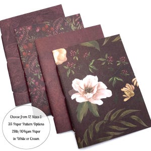 May include: A stack of notebooks with floral patterns in shades of burgundy and brown. One notebook features a large white and pink flower. The text on the image reads: "Choose from 12 Sizes & 35 Paper Pattern Options 28lb/104gsm Paper in White or Cream."