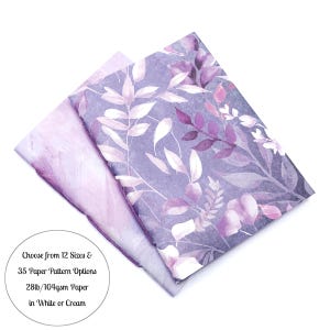 May include: Two sheets of paper, one with a watercolor floral pattern in shades of purple and white, the other with a marbled design. Text reads: "Choose from 12 Sizes & 35 Paper Pattern Options 28lb/104gsm Paper in White or Cream."