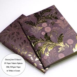 May include: Two notebooks with purple covers featuring a gold foil botanical leaf and flower pattern. A circular white label on the image contains the text: Choose from 12 Sizes & 34 Paper Pattern Options 28lb/104gsm Paper in White or Cream.