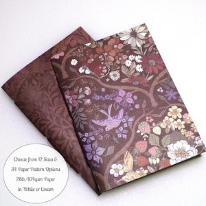 May include: Two sheets of paper with a dark brown background featuring a floral and bird pattern in shades of pink, purple, and cream. A circular white label displays the text: Choose from 12 Sizes & 34 Paper Pattern Options 28lb/104gsm Paper in White or Cream.
