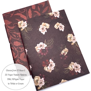 May include: Two notebooks with floral and patterned covers. One notebook has a dark burgundy cover with a repeating floral design. The other notebook has a dark brown cover with a floral pattern of white and burgundy flowers. The text on the image says "Choose from 12 Sizes & 35 Paper Pattern Options 28lb/104gsm Paper in White or Cream."