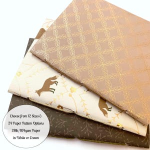 May include: Three notebooks with different patterned covers. The top cover is a light brown with a gold leaf pattern. The middle cover is white with a gold fox and floral pattern. The bottom cover is dark brown with a gold leaf pattern. The text on the bottom of the image reads "Choose from 12 Sizes & 24 Paper Pattern Options 28lb/104gsm Paper in White or Cream".