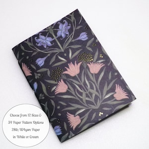 May include: A rectangular notebook with a dark purple cover featuring a floral pattern of blue and pink flowers with green stems. Text on the cover reads: Choose from 12 Sizes & 34 Paper Pattern Options 28lb/104gsm Paper in White or Cream.
