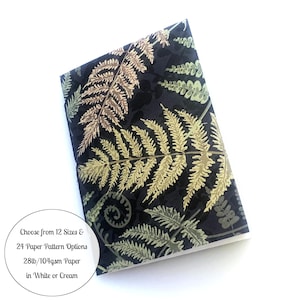 May include: A black notebook with a fern pattern in shades of green, brown, and gold. The text on the notebook reads "Choose from 12 Sizes & 24 Paper Pattern Options 28lb/104gsm Paper in White or Cream".