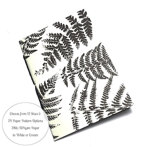 May include: A notebook with a fern pattern on the cover. The cover is white with black fern silhouettes. The text on the cover reads "Choose from 12 Sizes & 24 Paper Pattern Options 28lb/104gsm Paper in White or Cream".