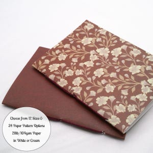May include: Two notebooks with stitched spines. The top notebook features a dark red cover with a light floral pattern. The bottom notebook has a solid dark red cover. A circular white label displays the text: Choose from 12 Sizes & 34 Paper Pattern Options 28lb/104gsm Paper in White or Cream.