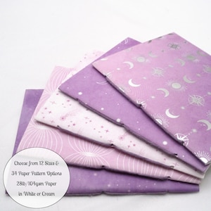 May include: A stack of purple and light pink paper sheets featuring celestial patterns of moons, stars, and suns. A circular white label on the bottom left displays the text: Choose from 12 Sizes & 34 Paper Pattern Options 28lb/104gsm Paper in White or Cream.