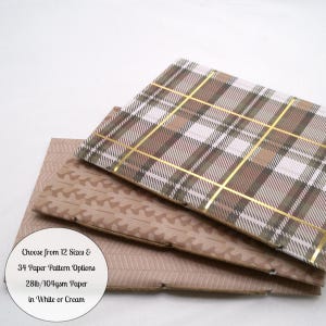 May include: Two rectangular sheets of paper stacked. The top sheet features a brown, white, and gold plaid pattern. The bottom sheet has a light brown herringbone texture. Text reads: Choose from 12 Sizes & 34 Paper Pattern Options 28lb/104gsm Paper in White or Cream.
