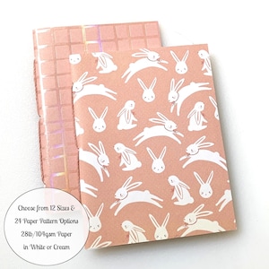 May include: Two pink notebooks with white bunny rabbit patterns. The notebooks are 28lb/104gsm paper and available in white or cream. Choose from 12 sizes and 24 paper pattern options.