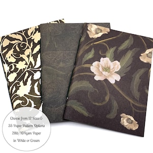 May include: Three rectangular notebooks with distinct covers: one with a cream and dark brown swirling vine pattern, one with a dark gray moth print, and one with a dark brown background featuring light pink flowers and green leaves. Text reads: Choose from 12 Sizes & 35 Paper Pattern Options 28lb/104gsm Paper in White or Cream.