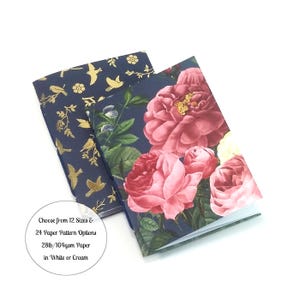 Peut inclure: Deux carnets avec des motifs floraux et d'oiseaux. L'un présente de grandes roses roses sur fond bleu foncé. L'autre a des oiseaux dorés et des accents floraux sur fond bleu foncé. Le texte sur l'image dit "Choisissez parmi 12 tailles et 24 options de motifs de papier 104 g/m² en blanc ou crème."