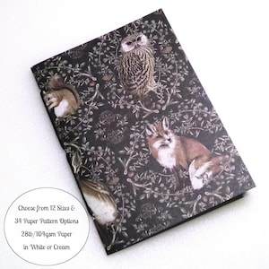 May include: A rectangular notebook with a dark black cover featuring a detailed woodland pattern of an owl, a fox, and a squirrel among branches. Text on the cover reads: Choose from 12 Sizes & 34 Paper Pattern Options 28lb/104gsm Paper in White or Cream.