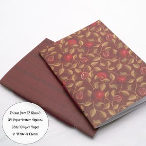 May include: Two notebooks with stitched spines. The top notebook features a dark brown cover with a repeating pattern of red pomegranates and tan leaves. The bottom notebook has a solid dark maroon cover. Text reads: Choose from 12 Sizes & 34 Paper Pattern Options 28lb/104gsm Paper in White or Cream.