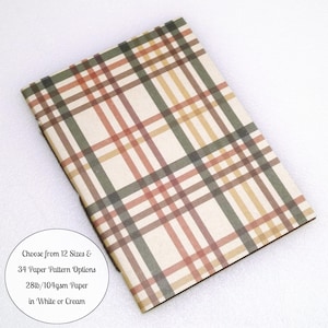 May include: A rectangular notebook featuring a plaid pattern in shades of olive green, tan, and muted red on a cream background. A circular white label includes the text: Choose from 12 Sizes & 34 Paper Pattern Options 28lb/104gsm Paper in White or Cream.
