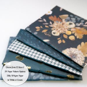 May include: A stack of five notebooks with stitched spines, featuring various dark blue and black covers with floral, leaf, and houndstooth patterns. Text on the image reads: Choose from 12 Sizes & 34 Paper Pattern Options 28lb/104gsm Paper in White or Cream.