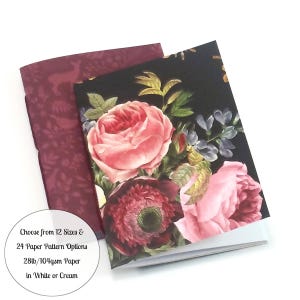 May include: Two notebooks with floral designs. The top notebook has a black cover with pink and red roses, while the bottom notebook has a burgundy cover with a deer pattern. The text on the bottom notebook reads "Choose from 12 Sizes & 24 Paper Pattern Options 28lb/104gsm Paper in White or Cream."