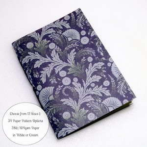 May include: A rectangular notebook featuring a dark purple cover with a repeating light gray botanical pattern of leaves and flowers. A circular white label on the cover reads: Choose from 12 Sizes & 34 Paper Pattern Options 28lb/104gsm Paper in White or Cream.