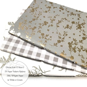 May include: Three sheets of wrapping paper in different patterns. The top sheet is gray with a gold floral pattern. The middle sheet is gray and white gingham. The bottom sheet is white with a green floral pattern. The text on the bottom sheet reads: "Choose from 12 Sizes & 24 Paper Pattern Options 28lb/104gsm Paper in White or Cream"