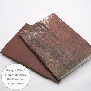 May include: Two notebooks with stitched spines. One has a solid dark brown cover, and the other features a photographic print of a forest with autumn foliage. A circular white label includes the text: Choose from 12 Sizes & 34 Paper Pattern Options 28lb/104gsm Paper in White or Cream.