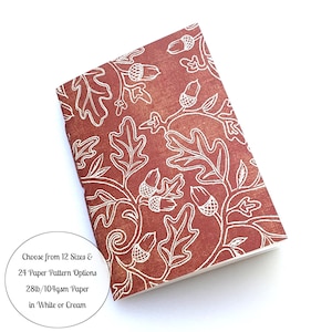 May include: A rectangular notebook with a rust-colored cover featuring a white oak leaf and acorn pattern. The text on the image reads: "Choose from 12 Sizes & 24 Paper Pattern Options 28lb/104gsm Paper in White or Cream."