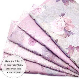May include: A stack of floral-patterned notebooks in shades of pink, purple, and gray. The notebooks feature a variety of flower designs and are bound with purple thread. The text on the image reads: "Choose from 12 Sizes & 35 Paper Pattern Options 28lb/104gsm Paper in White or Cream."
