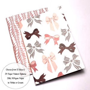 May include: Two sheets of wrapping paper with a bow pattern. The paper is white with pink and brown bows. The text on the paper reads "Choose from 12 Sizes & 24 Paper Pattern Options 28lb/104gsm Paper in White or Cream".