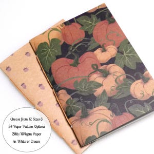 May include: A notebook with a dark background featuring orange pumpkins and green leaves, partially covered by a tan paper cover with a small brown acorn pattern. Text on the image reads: Choose from 12 Sizes & 34 Paper Pattern Options 28lb/104gsm Paper in White or Cream.