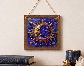 May include: A square wall hanging featuring a relief of a golden sun and crescent moon face set against a deep blue background with golden stars. The artwork is encased in a rustic brown wooden frame and suspended by a thin jute twine cord.