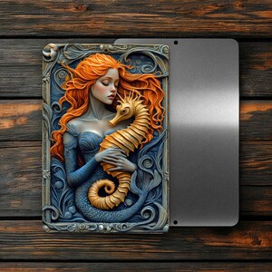 May include: A decorative metal panel featuring a mermaid with flowing orange hair embracing a golden seahorse. The mermaid is depicted in a blue dress with a blue tail. The panel has a detailed, ornate frame with a silver metal panel to the right.