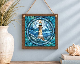 May include: A square wall hanging featuring a stained glass style illustration of a lighthouse surrounded by swirling blue and teal ocean waves. The artwork is set within a dark wooden frame and suspended by a natural fiber rope hanger.