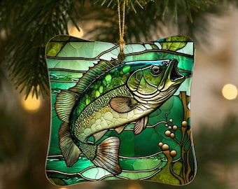 May include: A square-shaped hanging ornament featuring a stained glass style illustration of a green bass fish swimming among aquatic plants. The design uses various shades of green and gold with dark outlines, suspended by a thin gold cord.