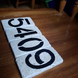 May include: Five white tiles with black numbers painted on them. The numbers spell out "60541".