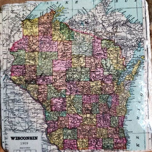 May include: A square stone coaster featuring a vintage 1909 map of Wisconsin. The map displays counties in shades of yellow, pink, and green, with black text labels for cities and regions. The text "WISCONSIN 1909" is printed in the bottom left corner.