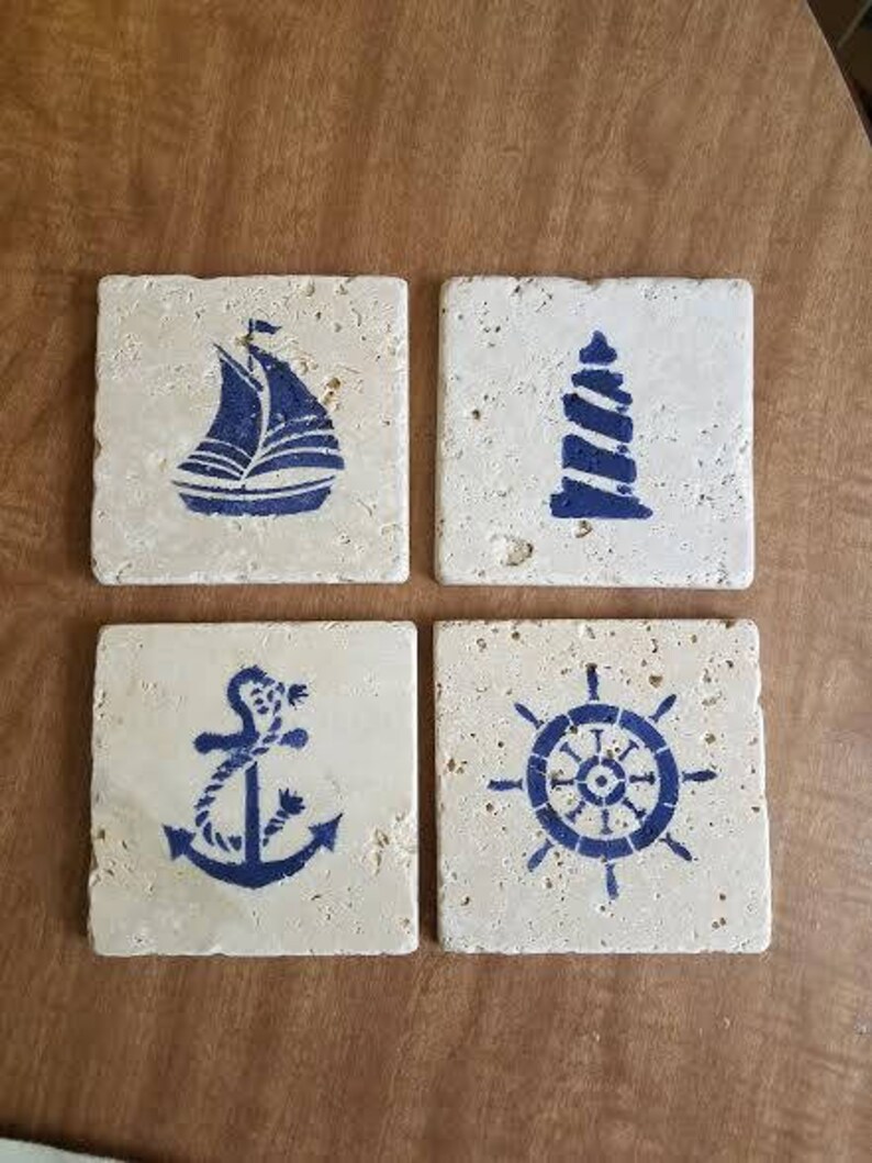 May include: Set of four square ceramic coasters with nautical designs. Each coaster features a different design: a sailboat, a lighthouse, an anchor, and a ship's wheel. The coasters are white with blue designs.