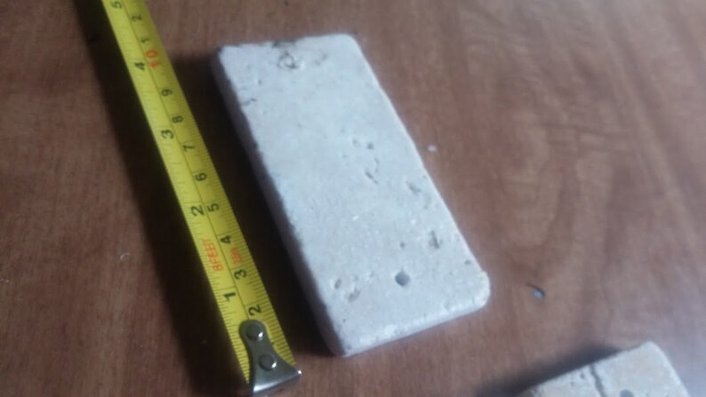 May include: A white rectangular tile with a rough texture and small holes. The tile is being measured with a yellow tape measure.