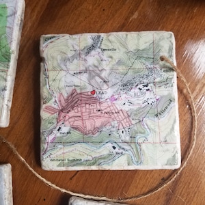 K&ouml;nnte beinhalten: Eine wei&szlig;e Keramikfliese mit einer Vintage-Karte von Lead, South Dakota. Die Karte ist in Braun, Gr&uuml;n und Rosa gedruckt. Ein rotes Herz ist &uuml;ber die Stadt Lead gelegt. Die Fliese hat ein Loch in der oberen Ecke und eine braune Schnur daran befestigt.