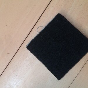 May include: A black square piece of fabric with a small loop of thread attached to one corner.