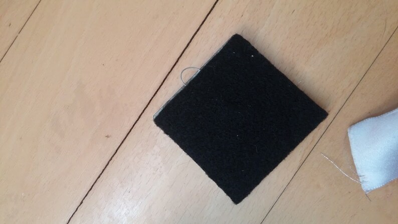 May include: A black square piece of fabric with a small loop of thread attached to one corner.