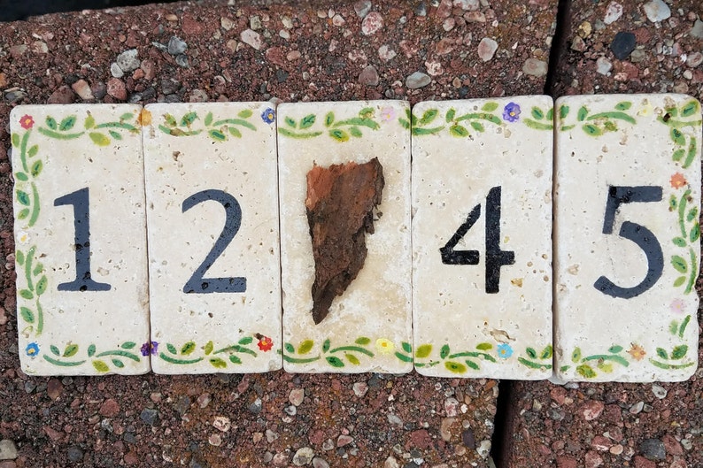 May include: Five ceramic tiles with a floral design border, each tile has a black number painted on it, the numbers are 1245, the tiles are arranged in a row.