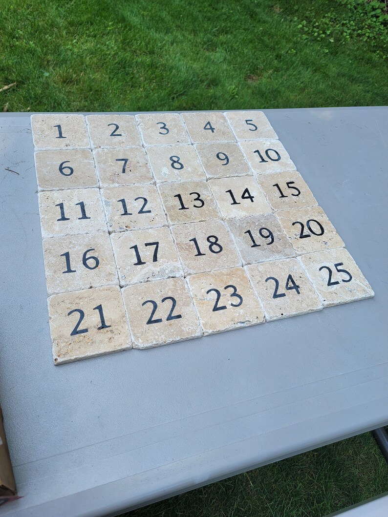 May include: A set of 25 beige square tiles with black numbers from 1 to 25. The tiles are arranged in a grid pattern.