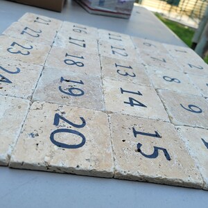 May include: A set of twenty-five beige stone tiles with black numbers from 1 to 25. The tiles are arranged in a row, with the numbers increasing from left to right.
