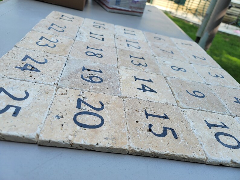 May include: A set of twenty-five beige stone tiles with black numbers from 1 to 25. The tiles are arranged in a row, with the numbers increasing from left to right.