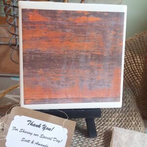 Puede incluir: Un posavasos de madera r&uacute;stico con un acabado naranja y marr&oacute;n desgastado. El posavasos est&aacute; en un peque&ntilde;o caballete con una etiqueta de agradecimiento que dice "&iexcl;Gracias! Por compartir nuestro d&iacute;a especial! Scott & Amanda".