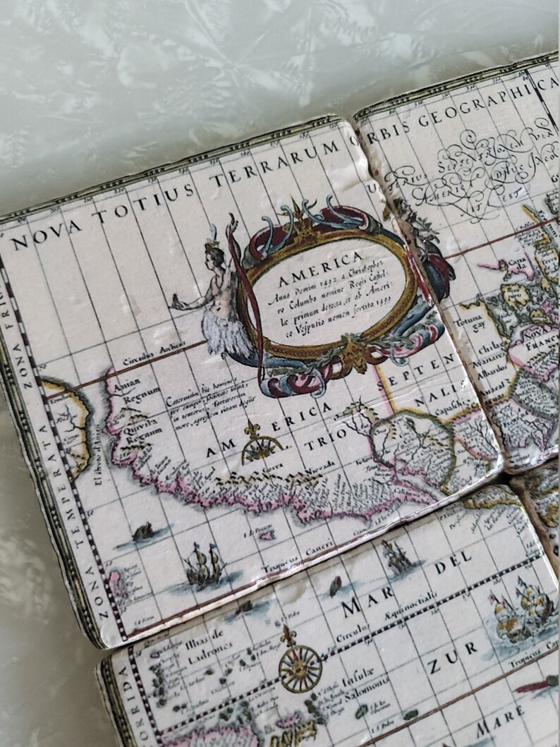 Puede incluir: Un juego de posavasos cuadrados con un dise&ntilde;o de mapa antiguo. Los posavasos presentan un fondo color crema con un mapa detallado de las Am&eacute;ricas, incluyendo texto e ilustraciones. El mapa est&aacute; enmarcado por bordes y texto decorativos.