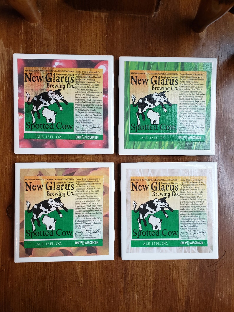 May include: Four white square coasters with a green, white and red design. Each coaster features a cartoon spotted cow jumping over the state of Wisconsin. The text "New Glarus Brewing Co." and "Spotted Cow Ale 12 fl. oz." is printed on each coaster. The text "Only in Wisconsin" is printed on the bottom of each coaster.