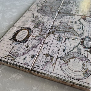 Puede incluir: Juego de cuatro posavasos cuadrados con un dise&ntilde;o de mapa del mundo vintage. Los posavasos tienen un fondo crema con ilustraciones detalladas de continentes, oc&eacute;anos y elementos cartogr&aacute;ficos en tonos marr&oacute;n, gris y morado. Los posavasos est&aacute;n hechos de un material duradero.